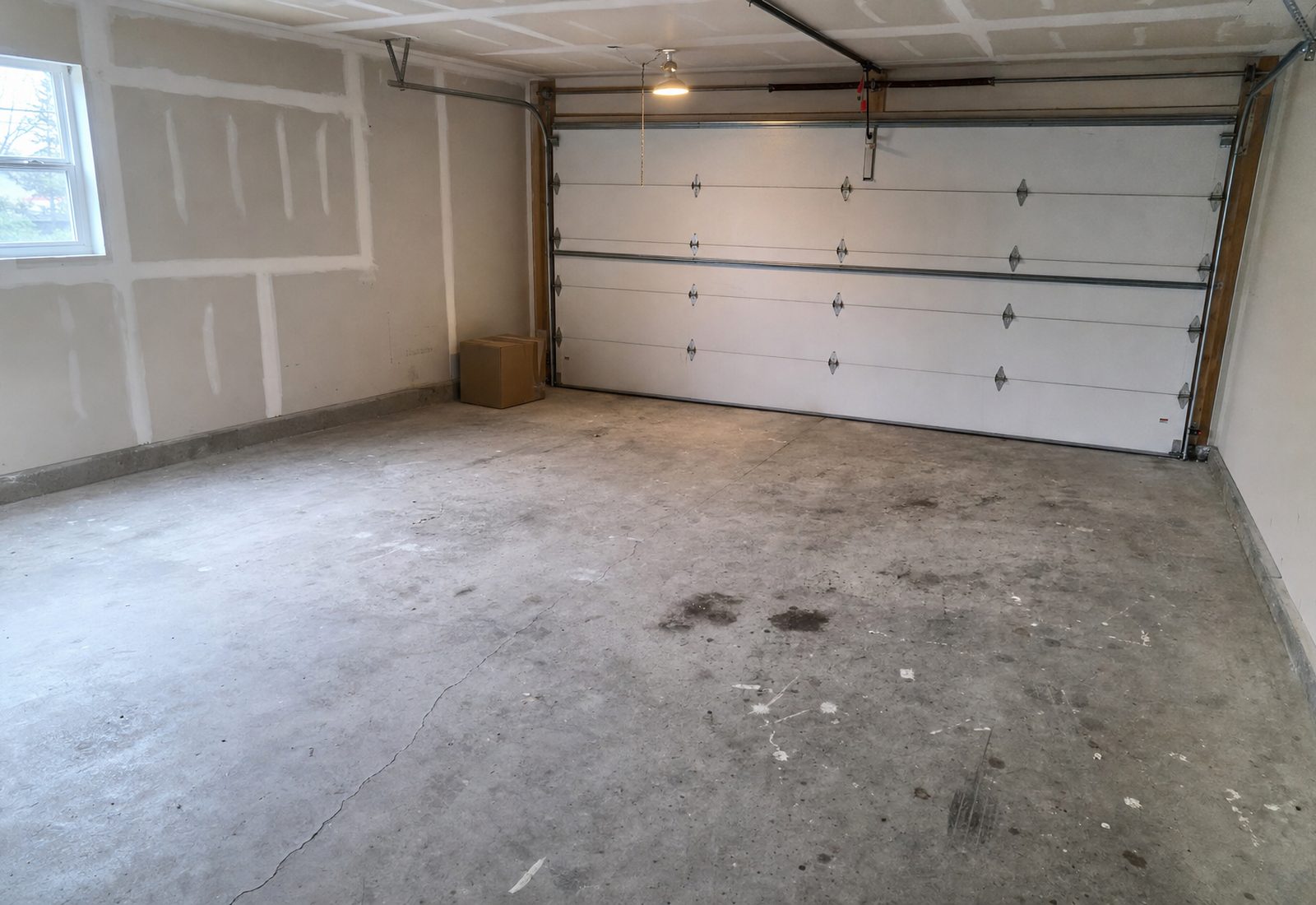 Bare garage concrete slab before coating, stained with oil spots, tire marks and a hairline crack