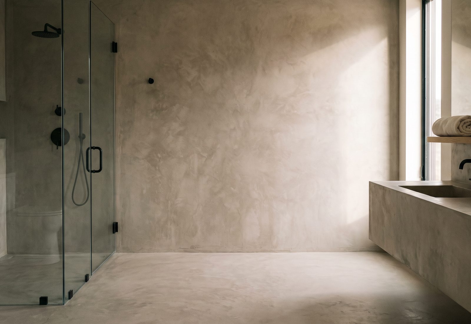 Finished micro cement bathroom with seamless warm greige walls, floor and floating vanity in a matte trowelled finish